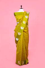 A lime green Banarasi silk saree with gold and silver zari kadhwa woven peacock motifs displayed on a mannequin against a pink background.