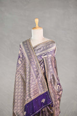 Purple Banarasi silk saree with silver-gold intricate woven patterns draped on a mannequin against a gray background