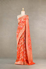 Orange Banarasi silk saree with light gold intricate peacock and birds woven patterns draped on a mannequin against a gray background