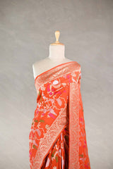 Orange Banarasi silk saree with light gold intricate peacock and birds woven patterns draped on a mannequin against a gray background