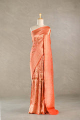 Orange Banarasi silk saree with light gold intricate woven patterns draped on a mannequin against a gray background