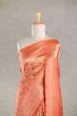 Orange Banarasi silk saree with light gold intricate woven patterns draped on a mannequin against a gray background