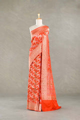 Orange silk saree with gold zari floral patterns on a mannequin against a gray background
