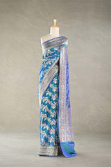 Teal blue Banaarsi silk saree with floral and meenakari zari work draped on a mannequin against a gray background