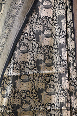Close-up of a patterned fabric with pichwai cow and swan designs on a dark background