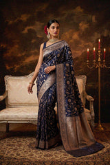 Woman in a blue saree with silver border standing in a room with a candlelit candelabra.