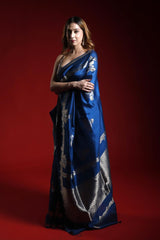 A woman wearing a blue party wear saree with silver patterns on a red background