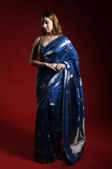 A woman wearing a blue party wear saree with silver patterns on a red background