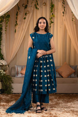 A woman in a blue traditional frock suit with a matching dupatta, standing in a decorated indoor setting.