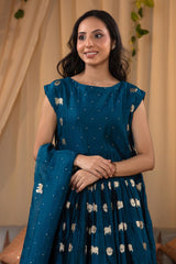 A woman in a blue traditional frock suit with a matching dupatta, standing in a decorated indoor setting.