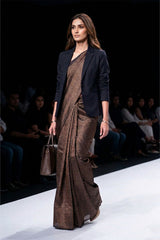 Model walking on a runway wearing a brown saree with a black blazer.