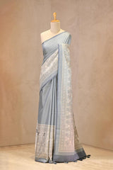 Close up of powder blouse Semi-Silk Saree showing water gold zari butis on the body and a Madhubani printed border featuring folk-art figures.