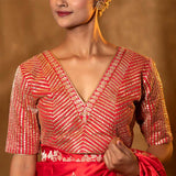 A woman wearing a red Katan silk Banarasi blouse with Gota Patti and Cutdana stripes, featuring a V-shaped neckline and half sleeves.