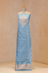 Light blue dress material with zari weavig on a mannequin against a beige background