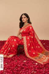 Woman in a red Banarasi saree with gold patterns sitting on a bed of red rose petals.