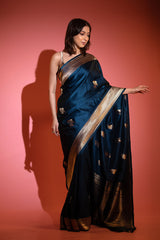 Woman wearing a dark blue saree with gold border against a red background