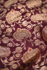 Close-up of a wine purple Banarasi silk fabric with intricate gold and silver floral patterns.