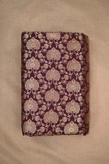 Close-up of a wine Banarasi silk fabric with intricate gold and silver floral patterns on beige background