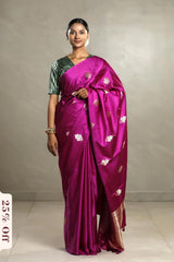 Woman wearing a vibrant purple saree with a green blouse against a plain background