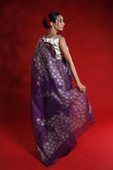 Woman wearing a purple saree with a white blouse against a red background