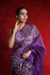 Woman wearing a purple saree with white patterns against a red background