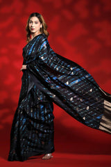 Woman wearing a black and blue party wear saree against a red background, black silk saree