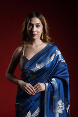 A woman wearing a blue party wear saree with silver patterns on a red background