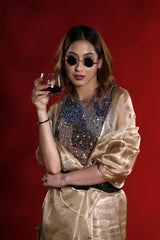 A woman in a gold outfit holding a glass of red wine, giving an aesthetic party wear look against a red background