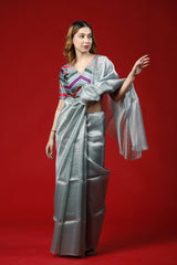 A woman wearing a blue-grey party wear saree dress for a cocktail party looks against a red background