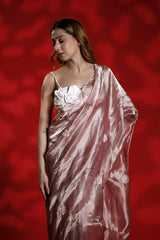 A woman wearing a pink party wear saree with a floral blouse against a red background