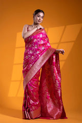 A woman modeling a pink Banarasi saree with gold zari woven floral buta and stripes, standing against an orange backdrop.