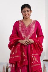 A woman in a traditional pink salwar suit and pink banarasi dupatta is standing in a decorated room.