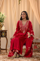 A woman in a traditional red salwar suit and red banarasi dupatta is situated in a decorated room.