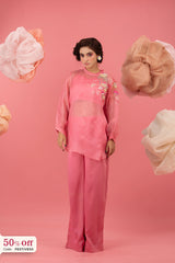 Woman in a pink outfit with floral embroidery against a pink background with decorative elements.