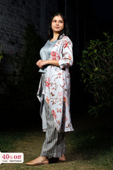 Woman wearing a floral kimono-style jacket over a light blue top and striped pants, standing against a dark background.