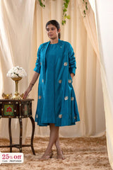 Woman wearing a blue dress with gold embroidery standing next to a decorative table with flowers.