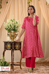Woman wearing a red patterned kurta with pink pants standing next to a decorative table with flowers.