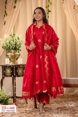 Woman in a red traditional outfit with gold patterns standing in a decorated room.