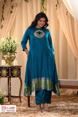 Woman wearing a blue traditional outfit with a decorative design, standing in a decorated room.