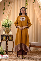 Woman wearing a mustard yellow dress with a decorative pattern, standing in a decorated room.