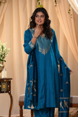A woman in a traditional blue salwar suit and blue banarasi dupatta is standing in a decorated room.