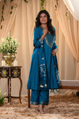 A woman in a traditional blue salwar suit and blue banarasi dupatta is standing in a decorated room.