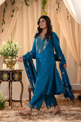 A woman in a traditional blue salwar suit and blue banarasi dupatta is standing in a decorated room.