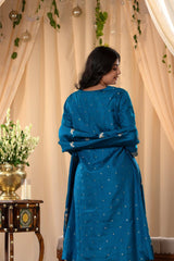 A woman in a traditional blue salwar suit and blue banarasi dupatta is standing in a decorated room.