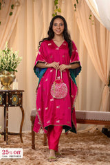Woman in a bright pink traditional outfit with a green jacket, standing in a decorated room.
