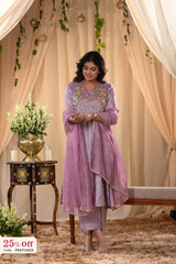 Woman in a pink traditional outfit standing in a decorated room with curtains and a table.