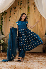 A woman in a blue traditional frock suit with a matching dupatta, standing in a decorated indoor setting.