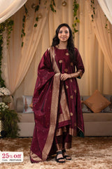 Woman in a maroon traditional outfit with gold details standing in a decorated room.