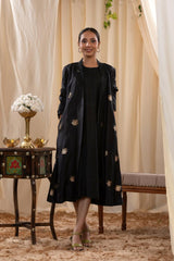 A woman in a black Indo-Western dress, paired with a matching coat featuring pichwai motifs.