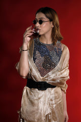 Woman in a gold outfit and sequined top drinking from a glass against a red background